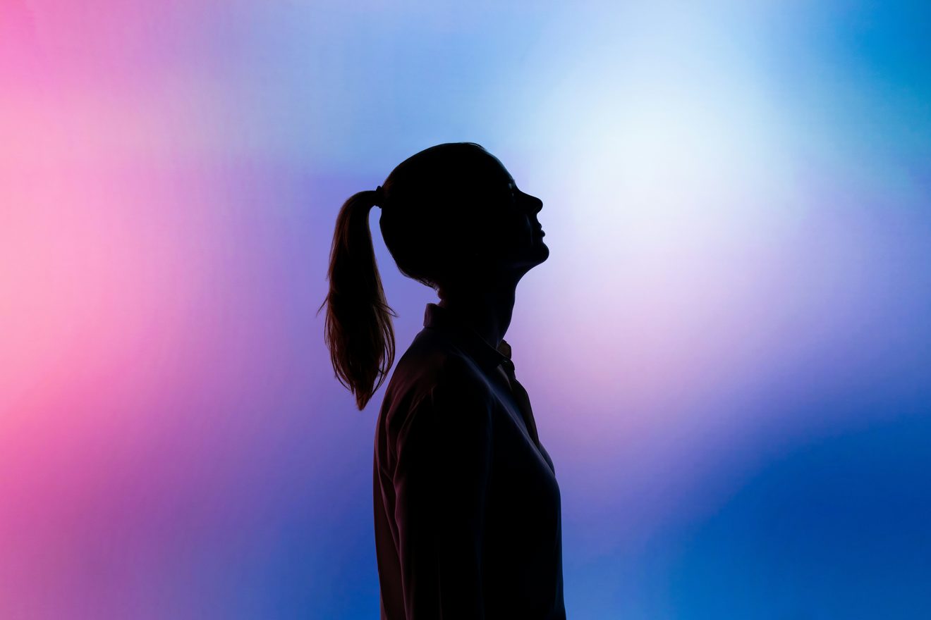 Profile silhouette of a person with a ponytail against a pink and blue gradient wall