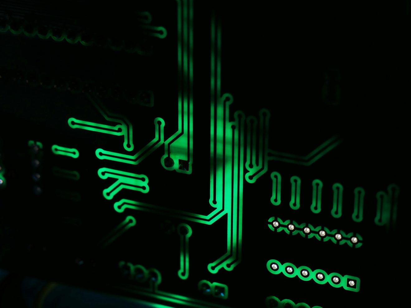 Glowing green conductive traces and solder pads on a dark circuit board