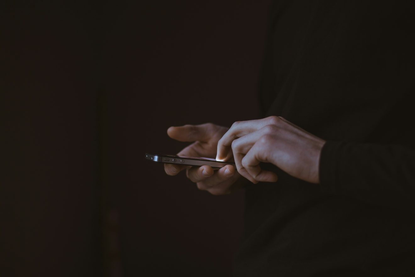 Two hands holding a mobile phone, lit faintly against a dark background