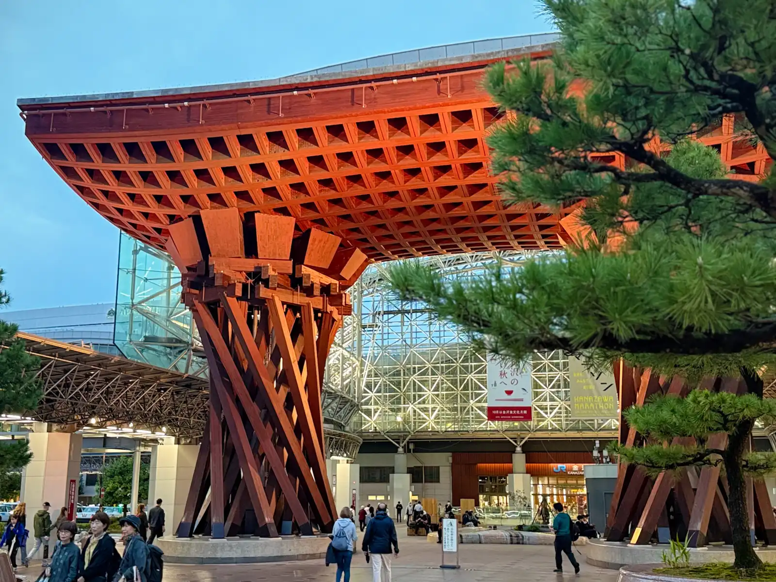 The Tsuzumi Gate in the evening, with the lights of the Motenashi Dome on behind it and a pine tree in the foreground.